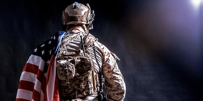 This is a photo of a soldier with an American flag draped over his back.