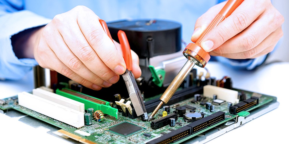 This is a photo of a computer technician replacing a capacitor on a printed circuit board (PCB).