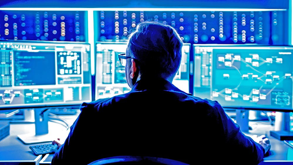 A man looking at three computer monitors