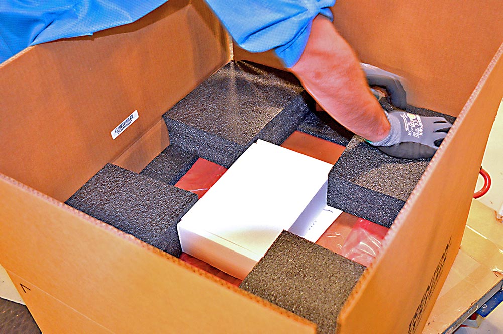 A Trenton Systems employee places the TMS4711 system in a cardboard shipping box and packs it with styrofoam