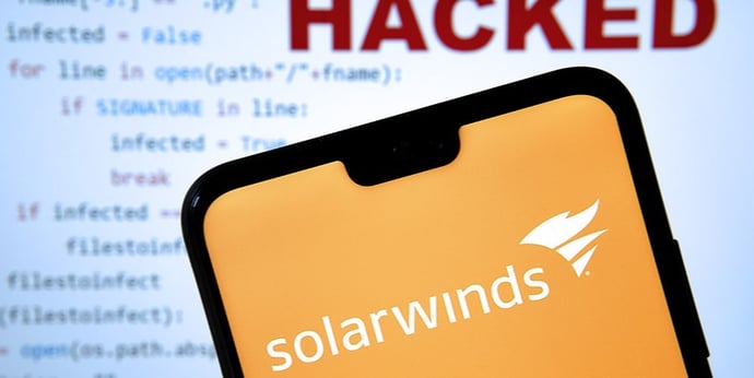 The SolarWinds app appears on a cellphone in front of a monitor that reads "hacked"