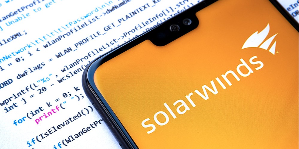 The SolarWinds app appears on a phone, which is laid upon a paper containing lines of code